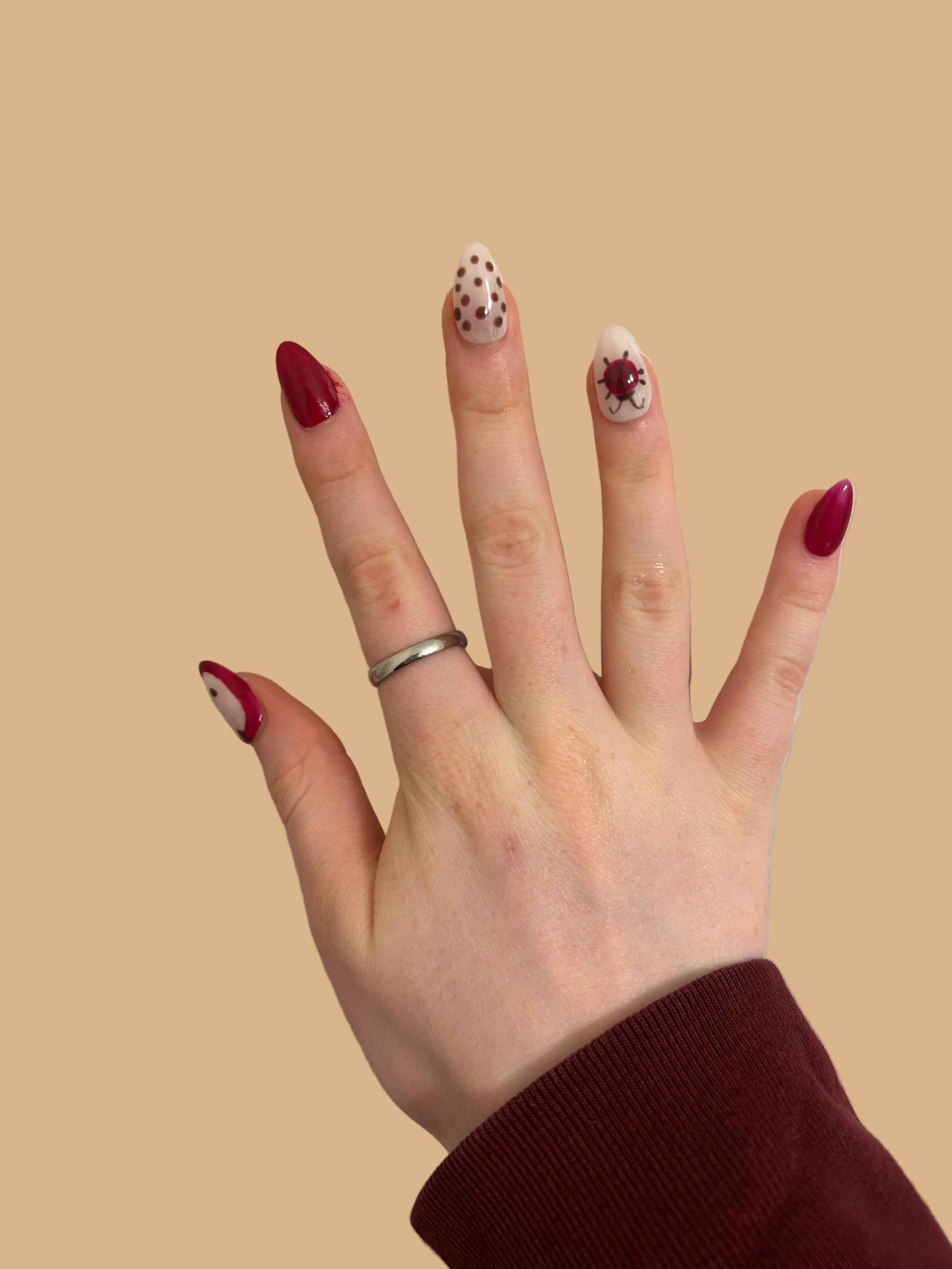 Hand with red nail polish and a ring on a beige background